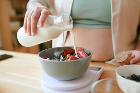 Fresh fruit and granola in bowl with milk being poured. Healthy breakfast being prepared, including strawberries and blueberries in mixの写真素材