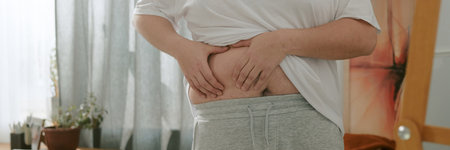 Person holding up shirt to view their stomach at home setting, possibly checking for health issues or physical changesの写真素材