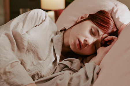Red-haired woman peacefully sleeping in soft light bedding, showcasing serene and relaxed mood....
