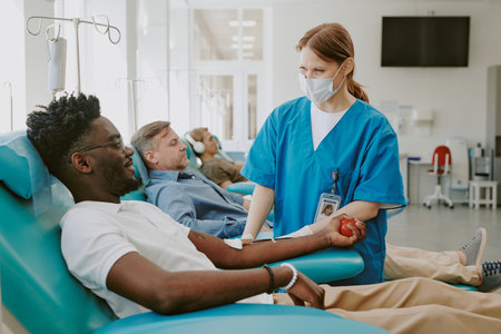 Young Black man donating blood while medical worker assisting, middle aged Caucasian man and young...