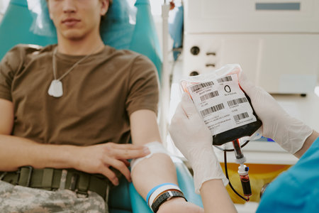 Caucasian teenage boy sitting in medical chair donating blood, while healthcare worker wearing...