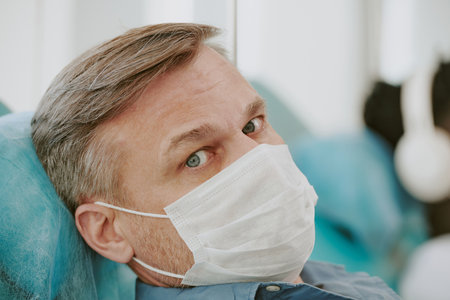 Portrait of middle aged Caucasian man wearing medical mask donating blood in clinical setting,...