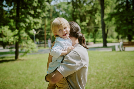Child smiling while being held by caring parent in park, child looking at camera with joyful...