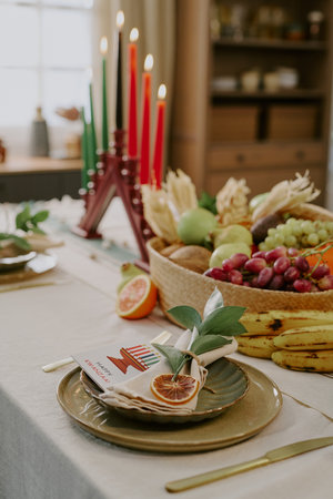 Kwanzaa table setting featuring kinara with seven lit candles, fruit basket with bananas, grapes,...