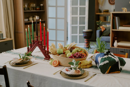 Kwanzaa table setting featuring kinara with seven candles, basket filled with assorted fruits and...