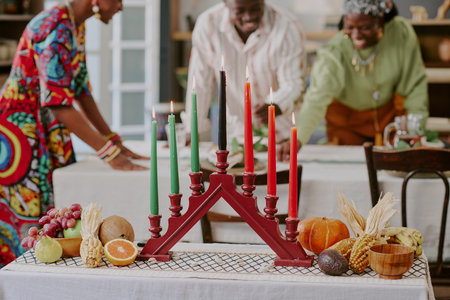 Three Black adults celebrating Kwanzaa, arranging festive table with kinara holding seven lit candles, assorted fruits, vegetables, and traditional decorations in foregroundの写真素材