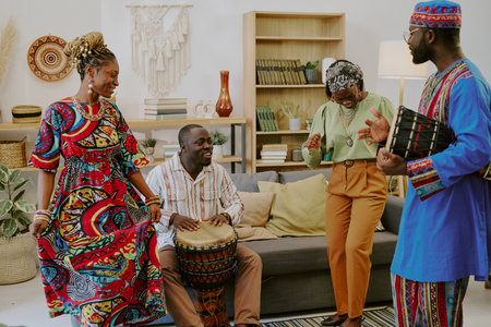 Group of Black adults celebrating Kwanzaa, playing traditional drums and dancing together in living room, smiling and enjoying cultural music, expressing joy and connectionの写真素材