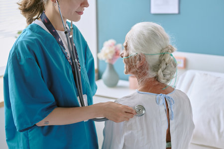 Caucasian female healthcare worker examining senior Caucasian woman with stethoscope in medical...