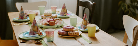 Birthday party table set with pastel plates, cups, party hats, donuts, marshmallows, pastries...