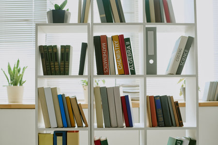Bookshelf standing in bright room holding textbooks and novels, including mathematics, chemistry,...