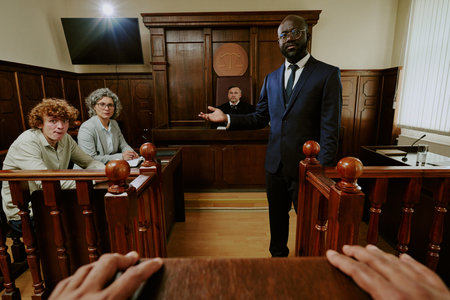 Black middle aged man in suit standing and gesturing in courtroom, Caucasian middle aged woman and...