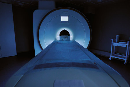 MRI scanner machine positioned in medical examination room with empty patient table extending toward large circular opening, clinical equipment visible in background, no people presentの写真素材