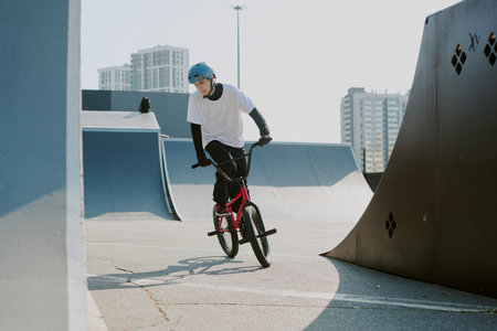 Teenage Caucasian boy riding BMX bike at skate park, wearing helmet and concentrating on maneuvering...
