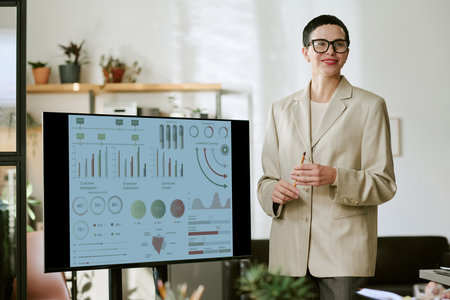 Caucasian middle aged woman standing beside digital display presenting business analytics charts and...