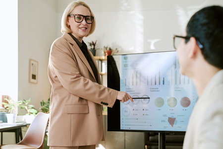 Caucasian middle aged woman presenting data on digital screen to young adult Asian man during...