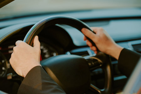 Middle aged man gripping steering wheel while driving modern car, hands positioned at ten and two, dashboard and part of interior visible in background, focus on actionの写真素材