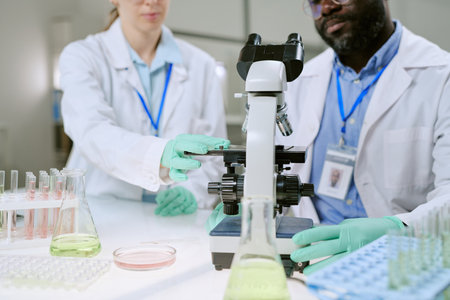 Caucasian woman and man working together in laboratory, adjusting microscope and handling glassware, conducting scientific research in medical environmentの写真素材