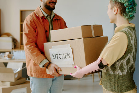 Young adult man and young adult woman with prosthetic arm carrying cardboard boxes labeled kitchen while moving into new home and doing renovations togetherの写真素材