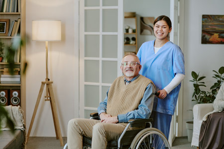 Caucasian senior man with disability sitting in wheelchair smiling while young adult Hispanic woman...