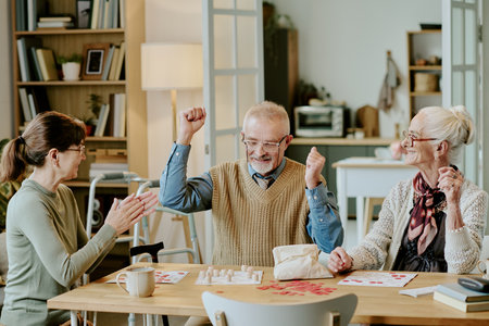 Senior Caucasian man celebrating victory with arms raised, while senior Caucasian woman and middle...