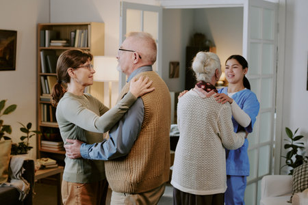 Senior Caucasian man and senior Caucasian woman dancing together, while another senior Caucasian woman dancing with young adult Hispanic female caregiver in living room settingの写真素材