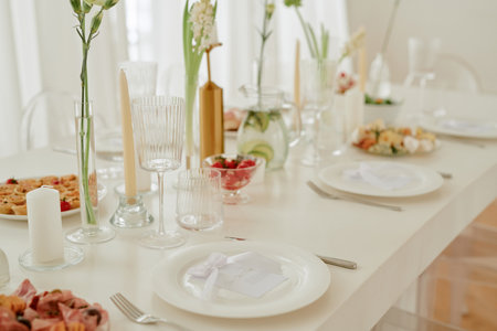 Wedding celebration table set with elegant glassware, plates, candles, floral arrangements and assorted appetizers, closeup showing place cards and festive food presentationの写真素材