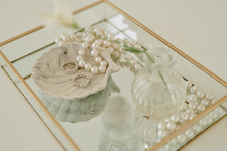 Closeup showing wedding rings and pearl necklace arranged on decorative tray with marble dish and glass vase, reflecting elegant bridal accessories for wedding celebrationの写真素材