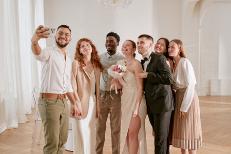 Group of young adult and middle aged multiethnic men and women standing close together smiling and posing for selfie during wedding celebrationの写真素材