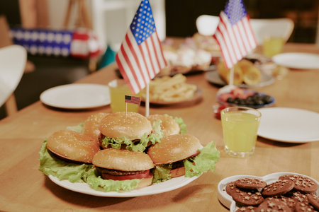 Plate of hamburgers with lettuce arranged on wooden table, small American flags inserted in buns,...