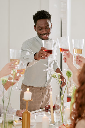 Young adult man smiling while toasting with group of people during wedding celebration, holding...