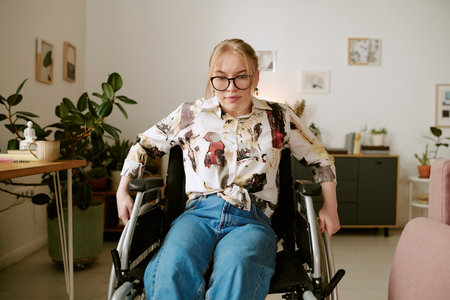 Portrait of young adult Caucasian woman with disability sitting in wheelchair indoors, wearing...
