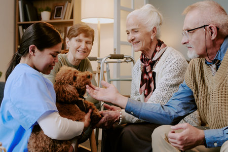 Senior Caucasian woman smiling while petting dog held by young adult Hispanic female caregiver,...