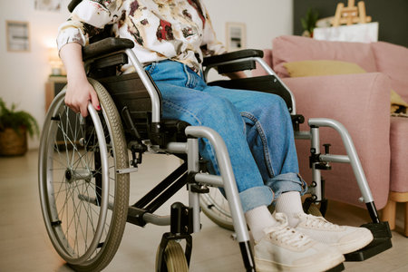 Woman with disability sitting in wheelchair indoors, hands gripping wheels, wearing casual clothing,...