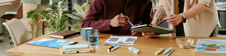 Caucasian young adult woman and Black young adult man collaborating at desk, reviewing documents and digital tablet, surrounded by office supplies and paperwork in modern workspaceの写真素材