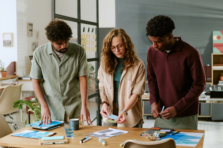 Young adult Caucasian woman collaborating with young adult Black man and young adult man of Middle Eastern descent, analyzing documents and discussing project at office tableの写真素材