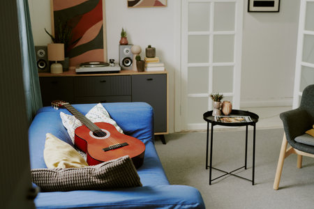 Acoustic guitar resting on sofa in modern living room, suggesting leisure activities at home, music recording, creative hobbies, home entertainment setupの写真素材