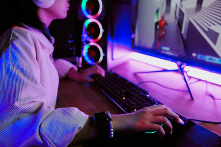 Teenage girl live streaming video games at home, wearing headphones and using gaming computer with...