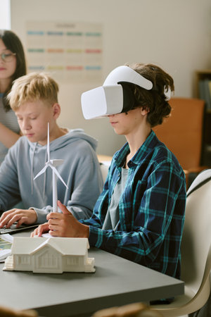 Caucasian teenage boy wearing virtual reality headset interacting with wind turbine model while...