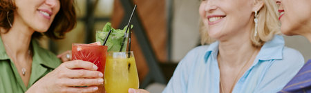 Website banner of three middle aged Caucasian women smiling and clinking glasses with colorful cocktails, sitting together at table, enjoying social gathering, faces partially visible, close upの写真素材