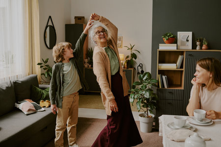 Senior Caucasian woman dancing with young Caucasian boy in living room while middle aged Caucasian...