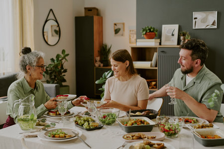 Senior Caucasian woman, young adult Caucasian woman, and young adult Caucasian man sitting at dining...