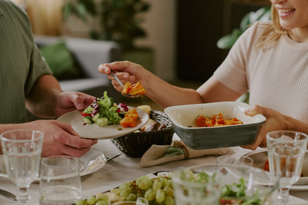 Caucasian young woman serving roasted vegetables onto plate held by Caucasian middle aged man during...