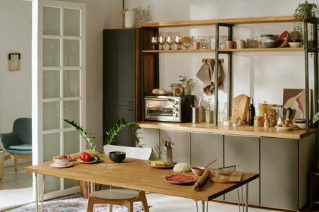 Modern kitchen interior featuring wooden table with various ingredients and utensils arranged for meal preparation, open shelving displaying glassware and kitchen accessoriesの写真素材