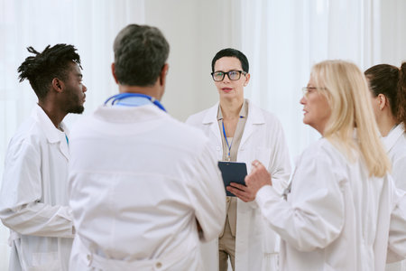 Group of diverse middle aged doctors standing in discussion, Caucasian woman with short dark hair holding clipboard leading conversation, medical professionals collaboratingの写真素材