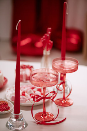 Closeup showing two pink cocktail glasses with red ribbon, tall red candles in holders, plate with heart shaped cookies and marshmallows on table, Valentines Day celebration sceneの写真素材