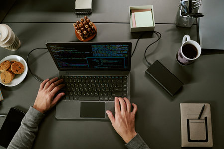 Young adult man working on laptop with external hard drive connected, hands typing code on keyboard,...