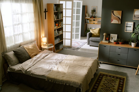 Modern bedroom interior featuring neatly made bed, decorative pillows, cozy blanket, bookshelf filled with books, potted plants, framed artworkの写真素材