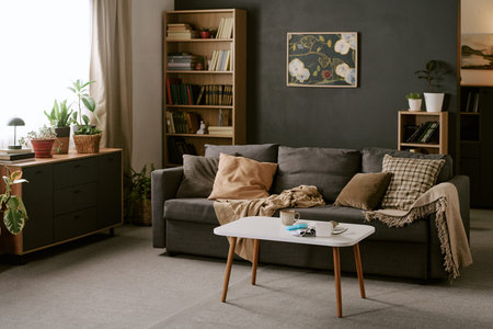 Modern living room interior featuring gray sofa with cushions and blanket, coffee table with...