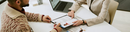 Website banner of man sitting at desk holding identification card while middle aged woman reviewing...