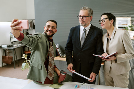 Young adult man taking selfie with middle aged man and young adult woman standing together in modern...